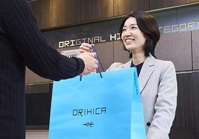 お客様に購入商品が入った紙袋をお渡ししているMさんの写真